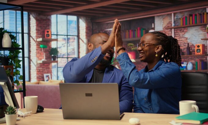 Black freelancing couple doing a high five to celebrate their achievement Two people celebrating a success together.